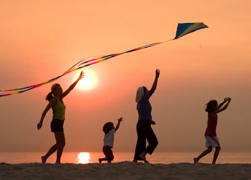 Family on beach at sunset, flying a kite
